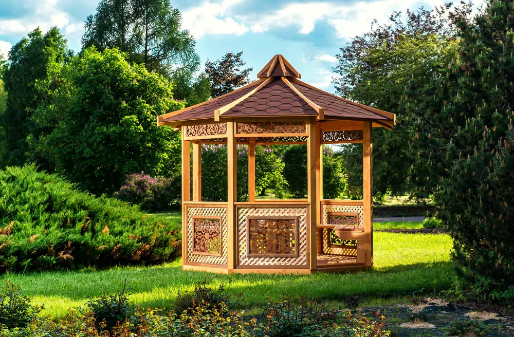 The obvious standout feature on this gazebo is the intricate wood carvings appearing on each side of the octagonal structure. Placed within the side fencing and between the support beams below the roof, these gorgeous carvings offer a unique bit of artistry in an unexpected place. The sumptuous roof design, with exposed beams, adds another layer of visual intrigue.