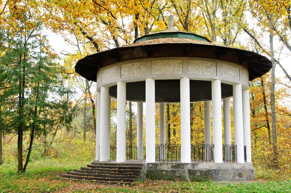 While we're used to seeing any and all manner of wooden gazebo designs, it's truly surprising to see one built from stone. This massive structure is wrapped in bespoke white pillars, supporting a tiered green roof over a concrete and stone base. Wrought iron fencing fills in the space between pillars, while the interior space is more than ample for a full dining party.