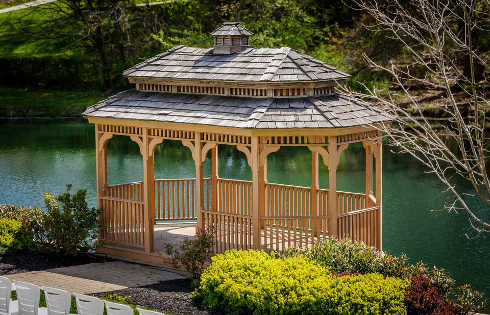 With its rich natural wood structure and weathered, rustic styled roof tiles, this gazebo could be at home on any traditionally styled home's property. What truly sets it apart, aside from its large, oval shaped design, is its placement near a body of water. It provides the perfect backdrop to an outdoor dinner, a relaxing day in the garden, or even a wedding.